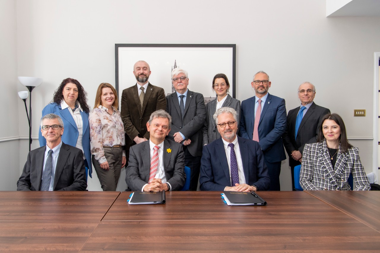11 people sitting and standing behind a table, including the Vice-Chancellors of the University of Sydney and the University of Glasgow. Documents sit on the table in front of them.