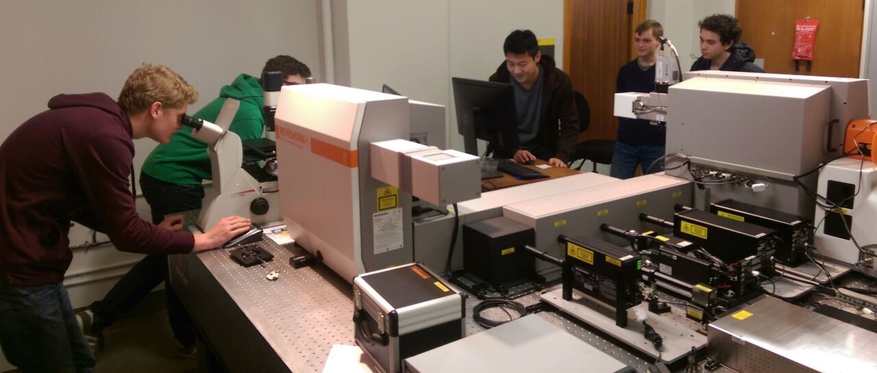 School students looking into microscopes and watching a computer monitor associated with the dual Renishaw Raman instrument.