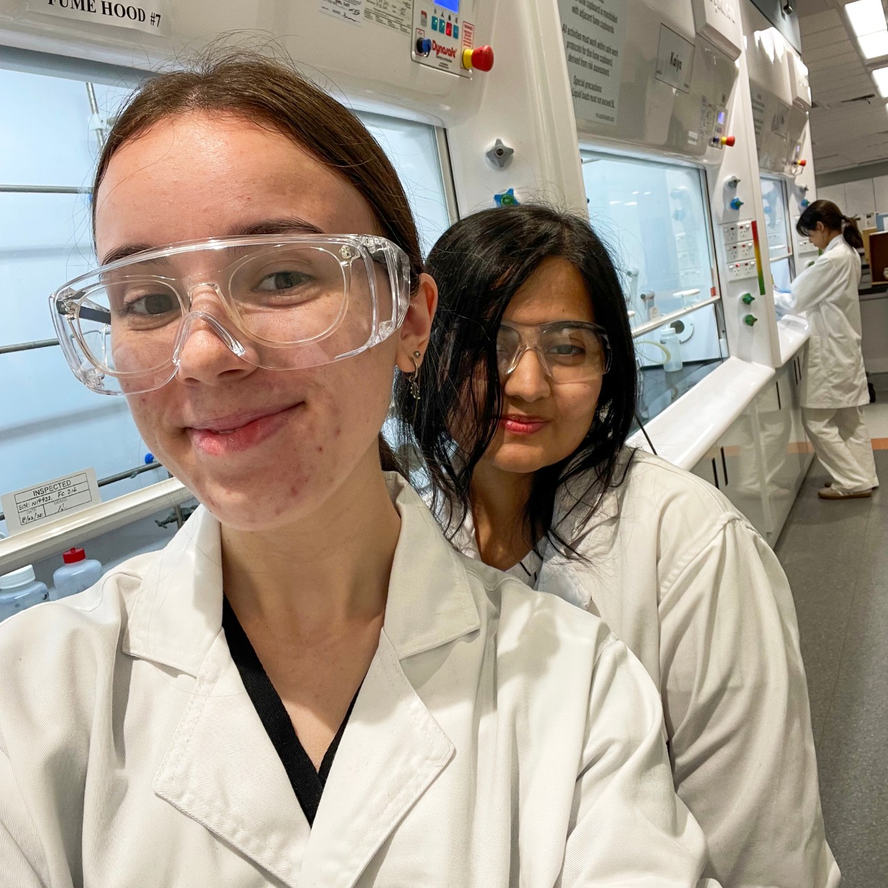 Cameryn Smider wearing goggles and lab coat with a fellow student in the lab.