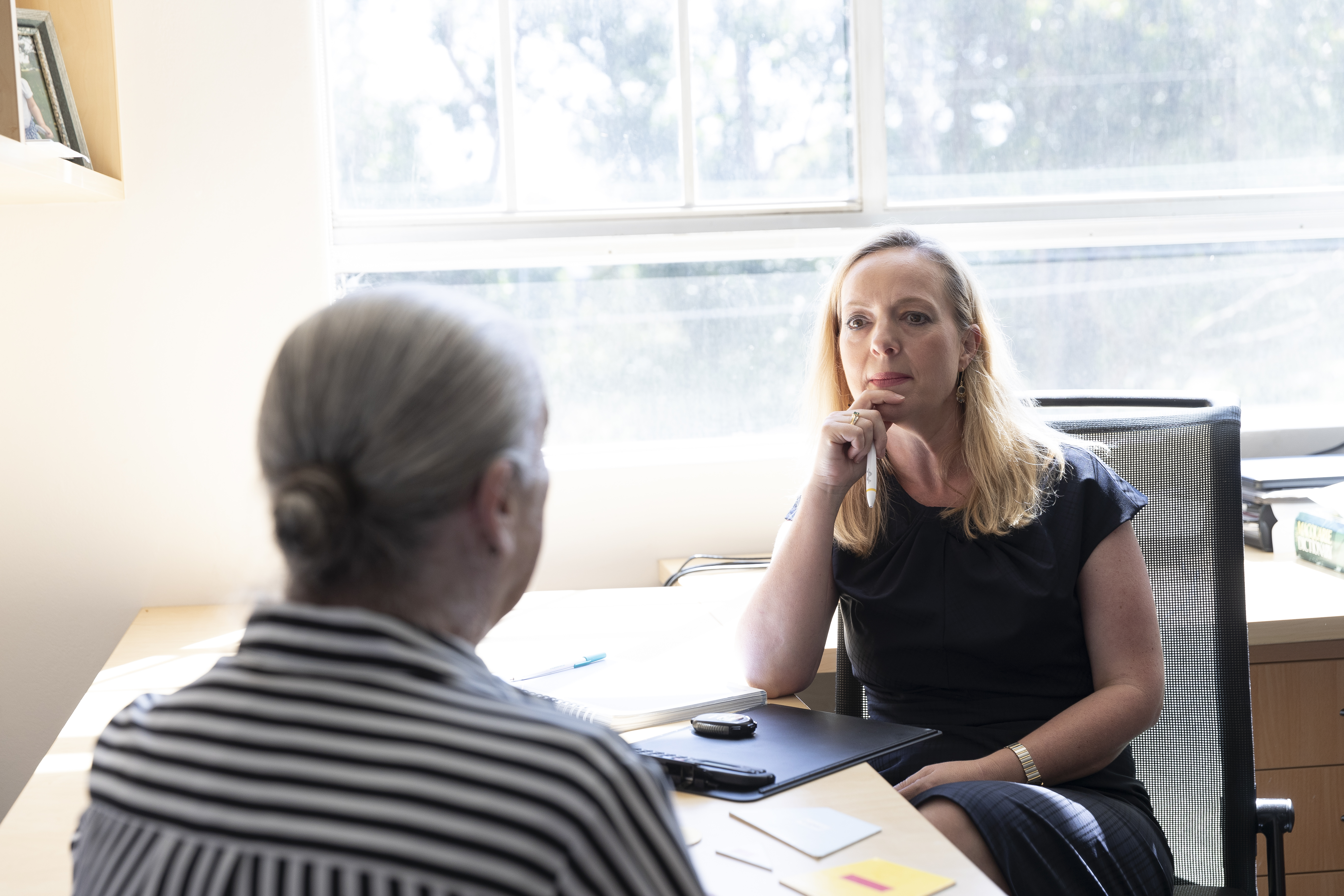 Professor Sharon Naismith sits at her desk listening to a patient who faces away from the camera