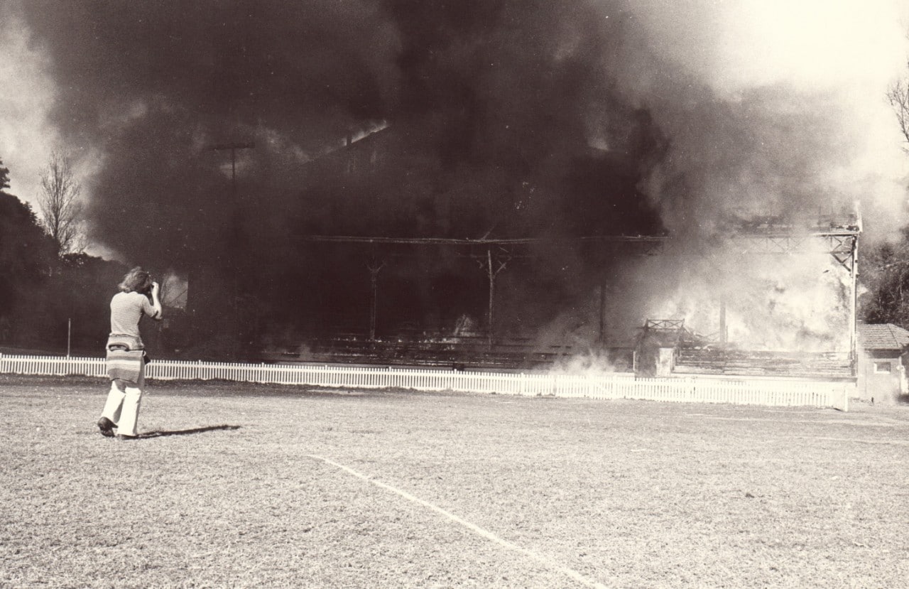 A black and white image of the grandstand on fire while a photogropher captures the moment