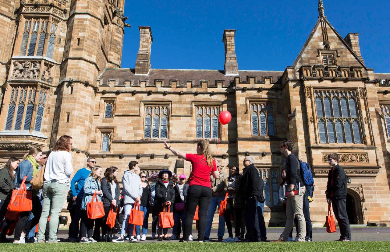 Student ambassador leading a group of visitors at Open Day on a campus tour in front of the Quadrangle