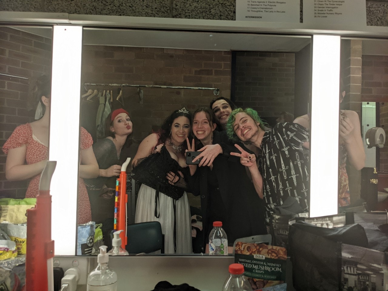 A group of performers smiling into a mirror backstage at a theatre