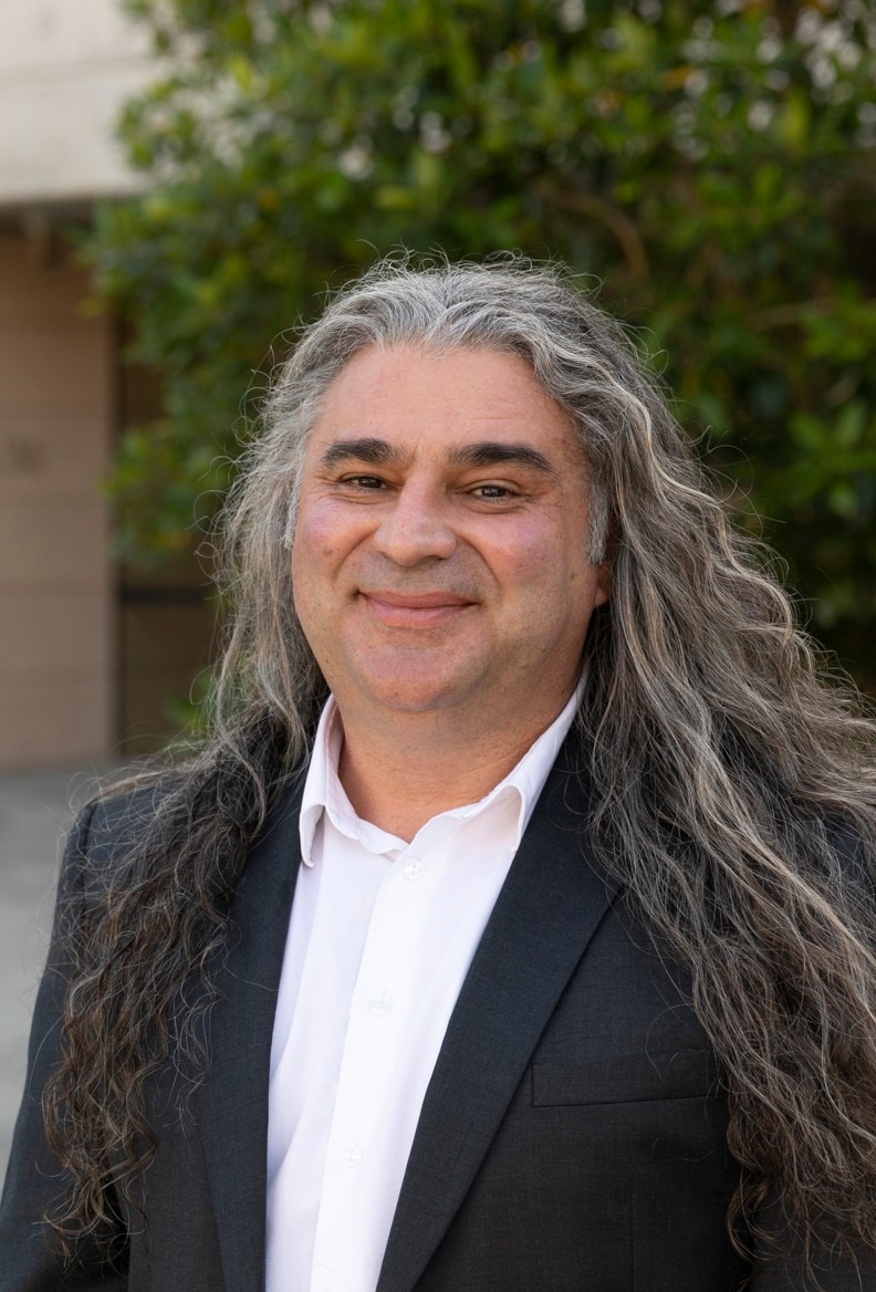 portrait of Michael standing out front of the Chau Chak Wing Museum, he has a smiling fce and long flowing black and grey hair