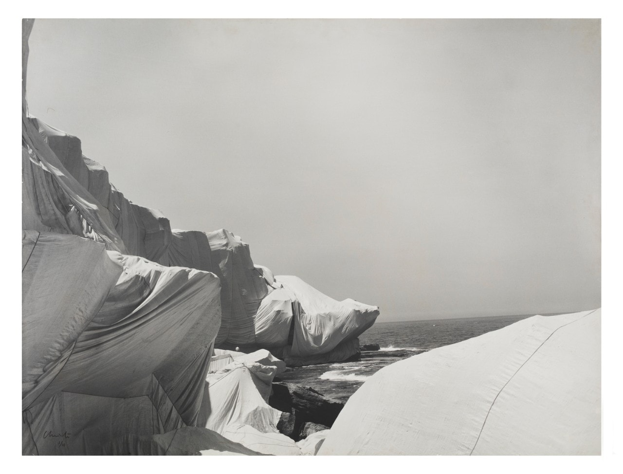 A black and white photograph of a rocky headland is wrapped in white material.