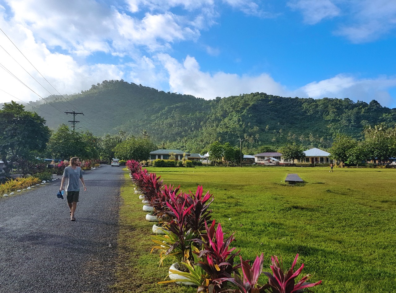 man walking down road in Samoan village with mountains in the distance 