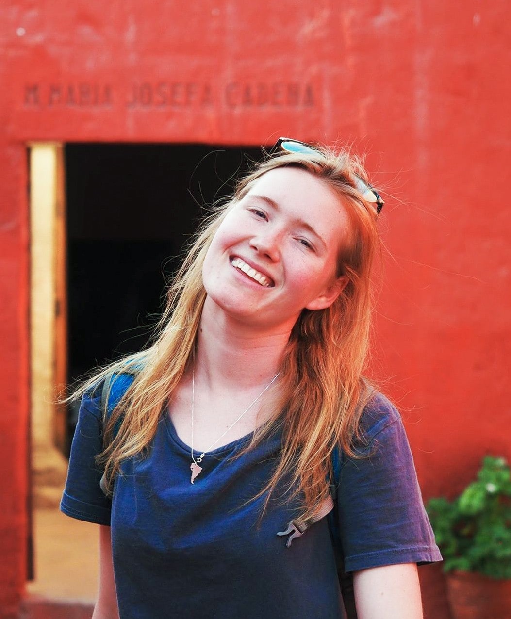 Picture of Madeleine Combe standing in front of a red wall, smiling