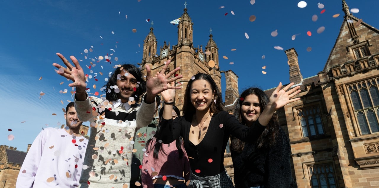 Group of students throw paper confetti in front of quadrangle in celebration