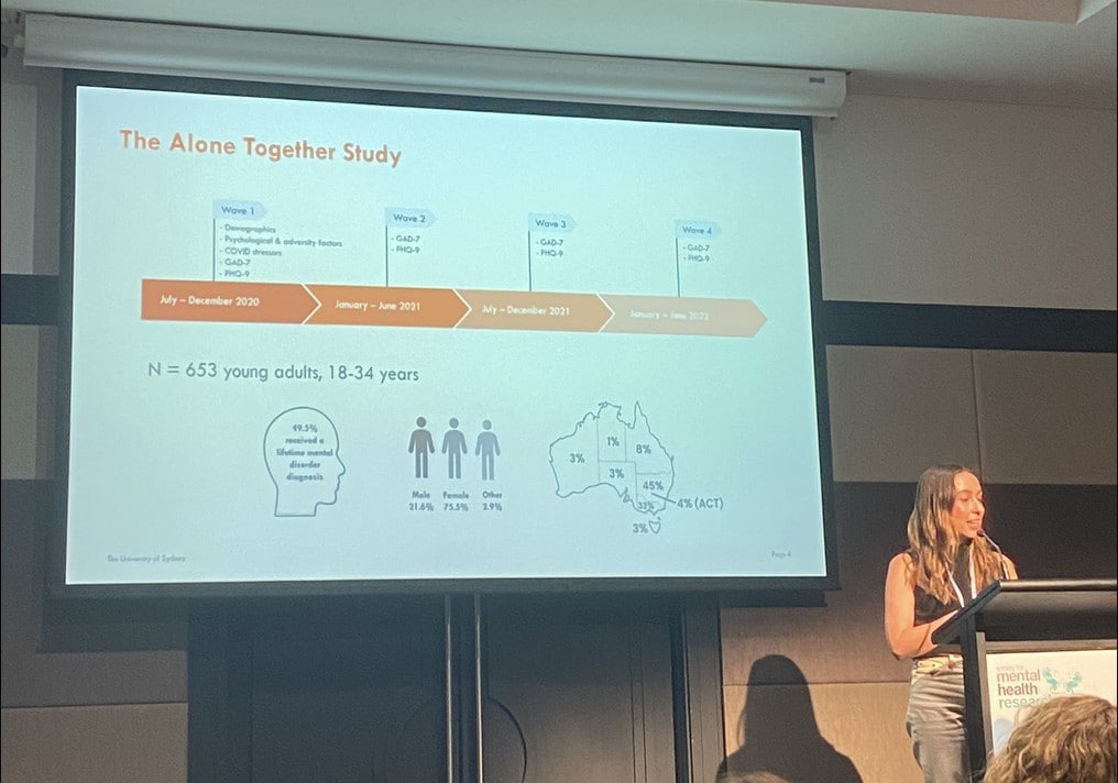 Amarina presents at the SMHR conference. She is standing behind a podium and is presenting on the Alone Together study.