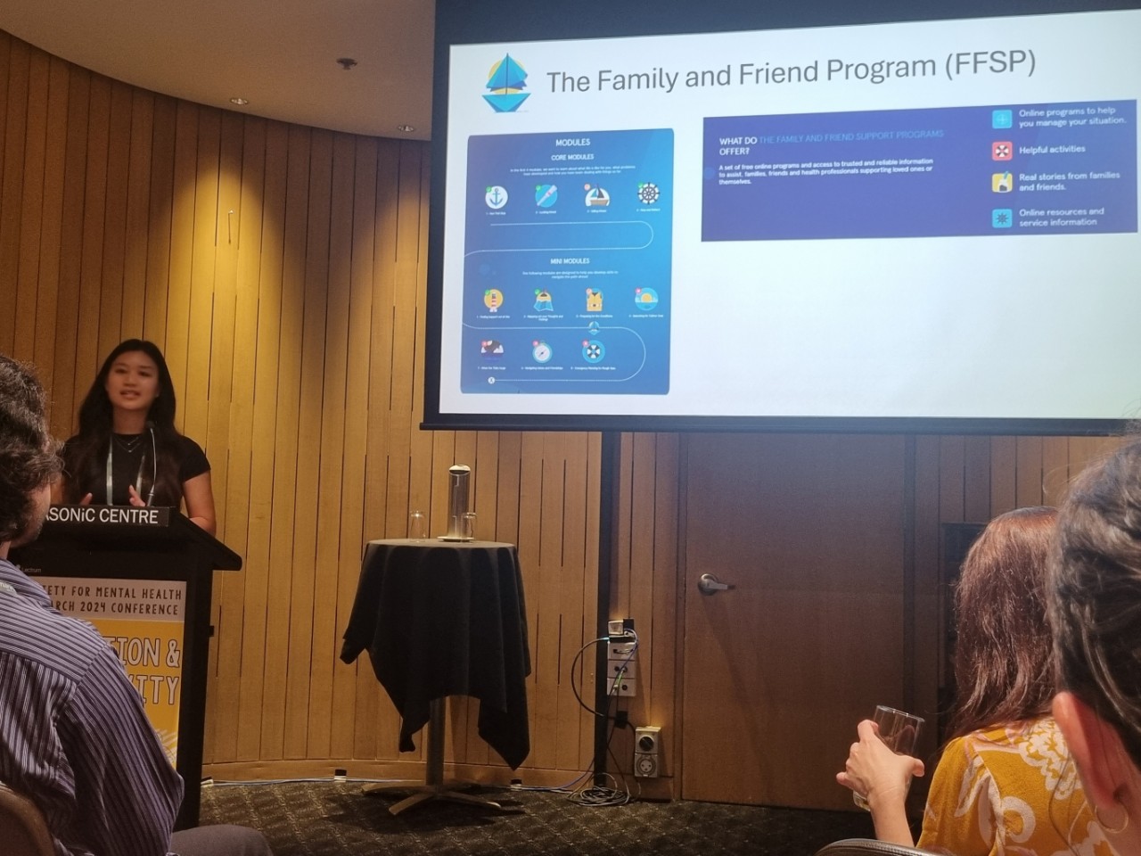 A woman standing next to a large screen, sharing information about the Family and Friends Support Program. 