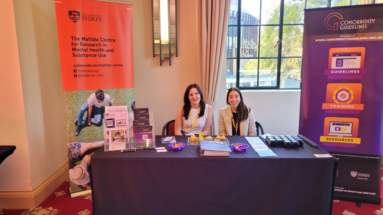 Two women sitting at a desk with the banner for the comorbidity guidelines in the background