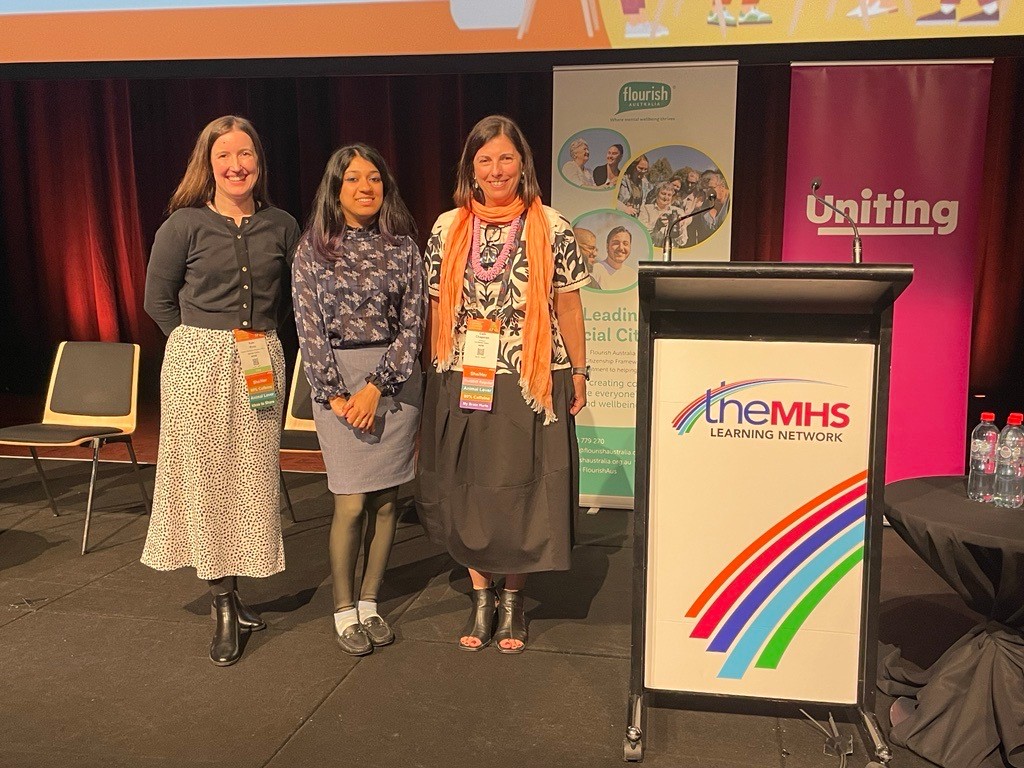 three women standing in front of a theMHS Conference pull up banner.