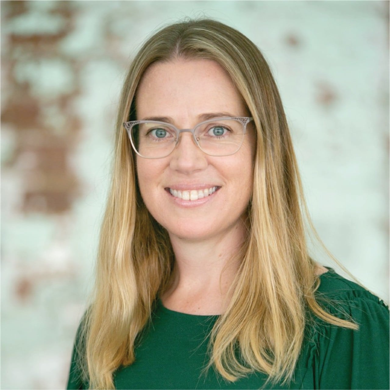 An image of Dr Erin Kelly. She is a blonde woman with shoulder-length hair, and is wearing clear frames and a plain green shirt.