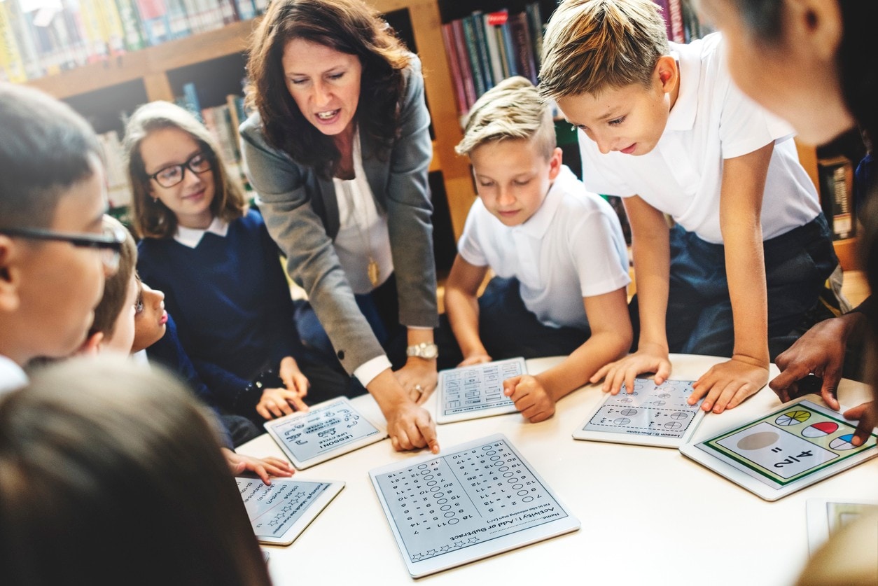 Young students and a teacher discuss maths at a desk. Image: iStock 