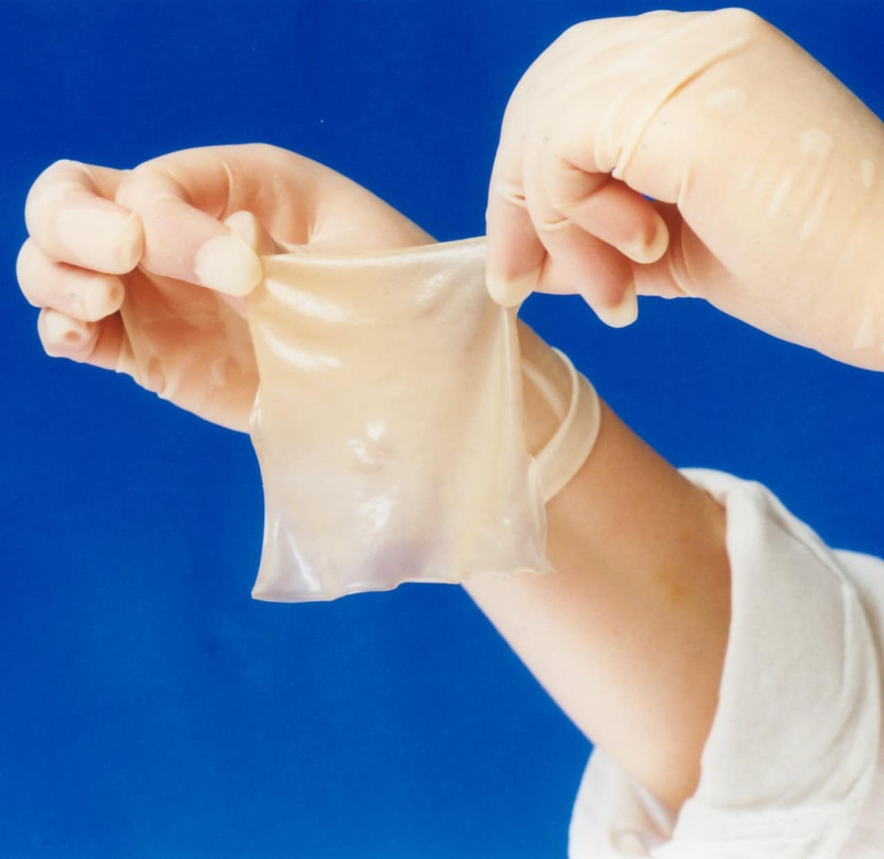 Gloved hands holding up elastin sheets for tissue repair.