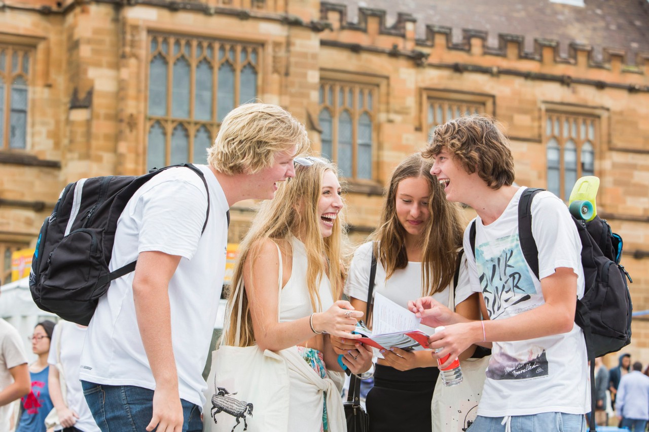 Four students outside the Quadrangle laughing 