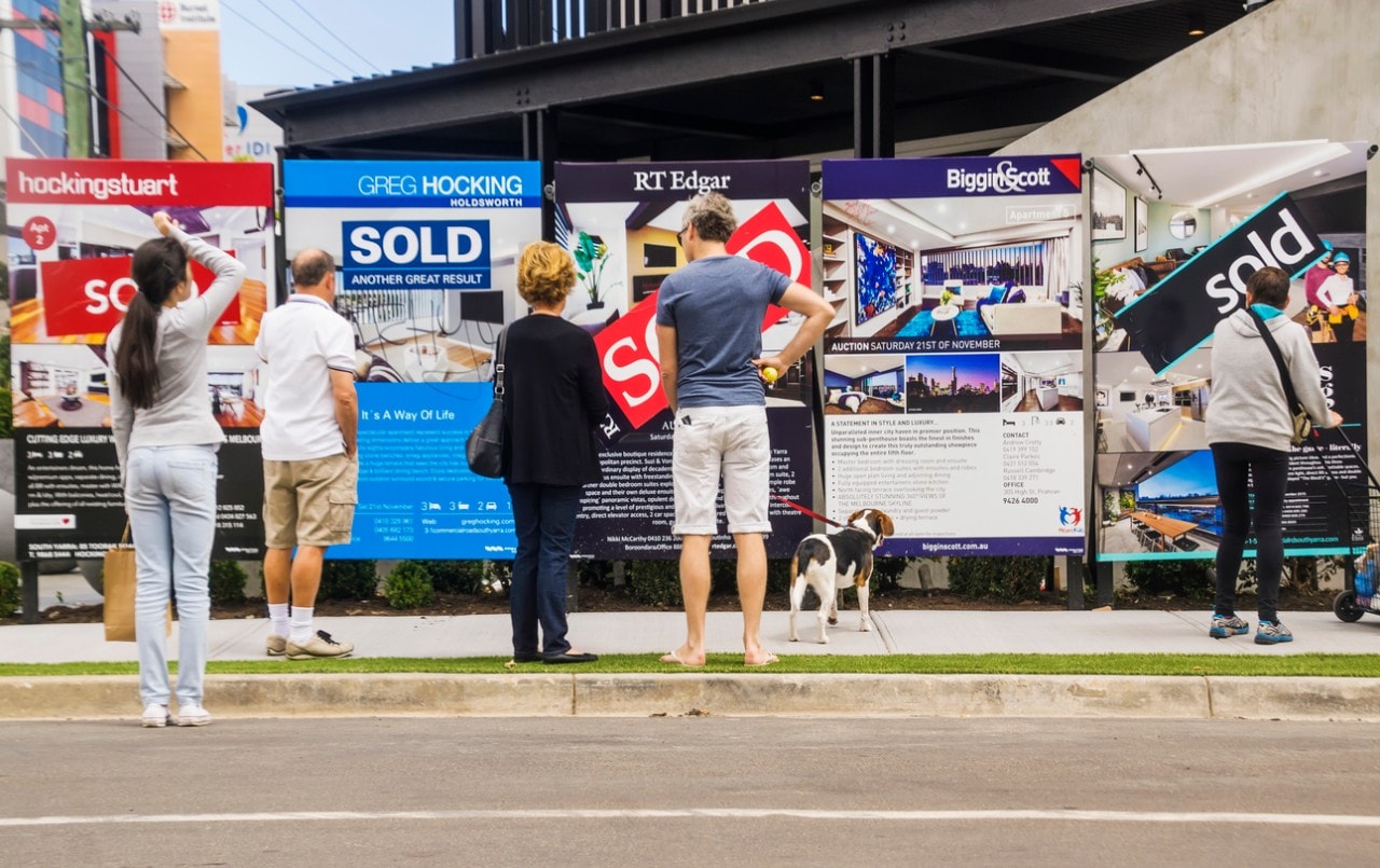 People reading a row of estate agent signs outside a newly-renovated apartment building in South Yarra, Melbourne.
