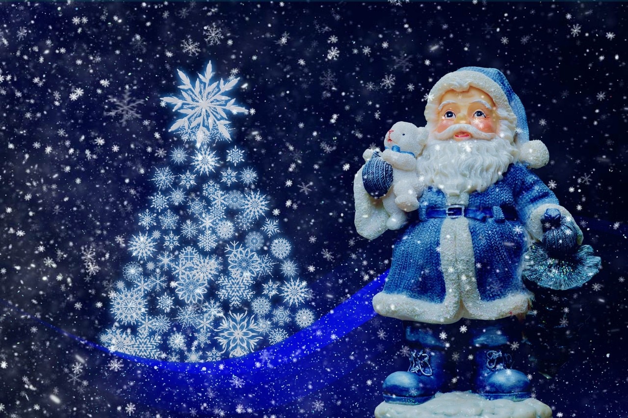 Santa wearing a blue suit standing next to a Christmas tree