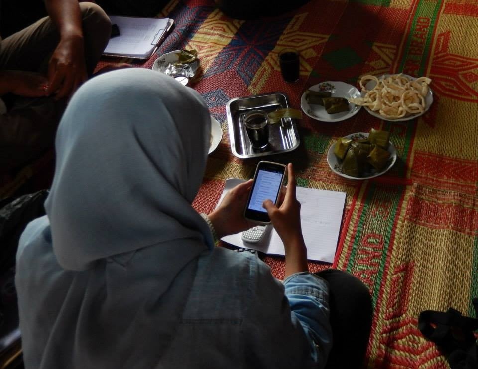 A research assistant using one of her phones during a break in interview with a farmer in his house in Sumatra. Photo from a survey supervised by Ayu Pratiwi. Photo: Petr Matous.