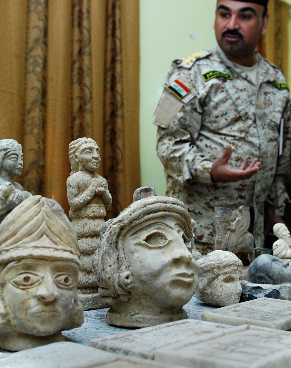 Iraqi colonel ali sabah standing next to artefacts - stone heads - retrieved after the looting