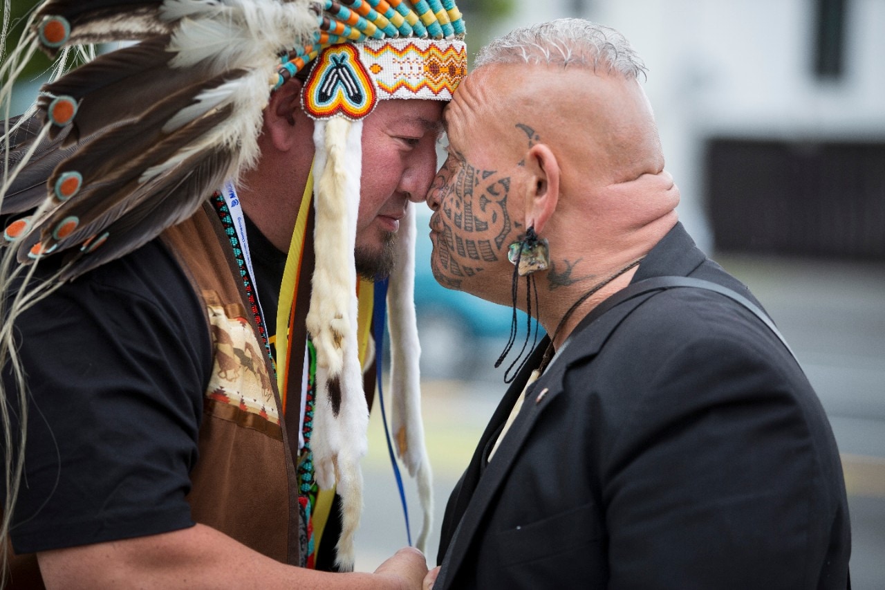 Two men, one wearing a traditional headdress, embracing