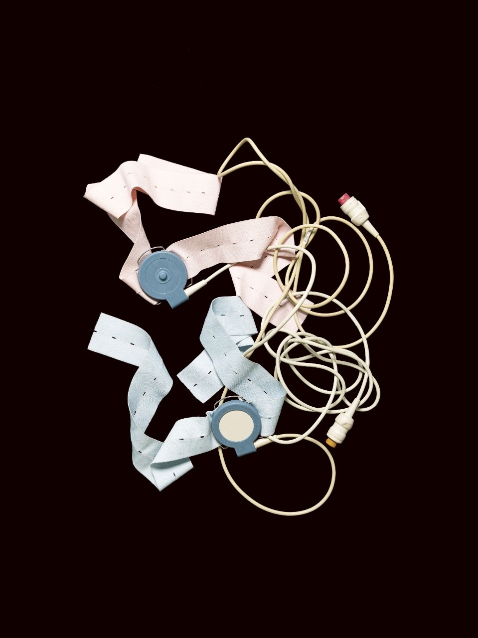 A tangle of blue and pink straps and wires. The outmoded cardiotocography monitor (known as a CTG), on a black background.