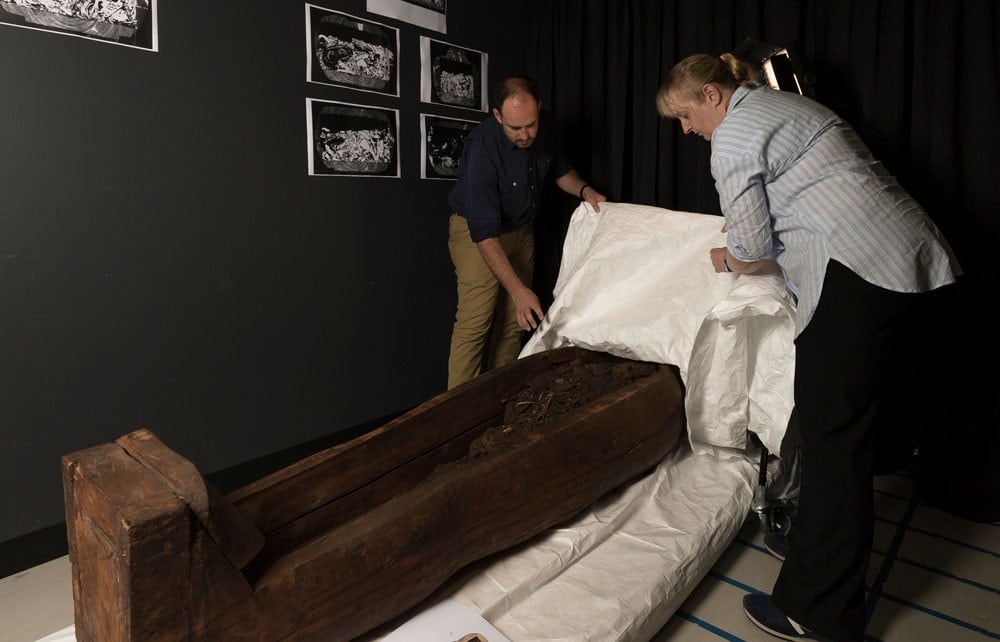 Fraser and Lord peel back a sheet to reveal the wooden mummy coffin