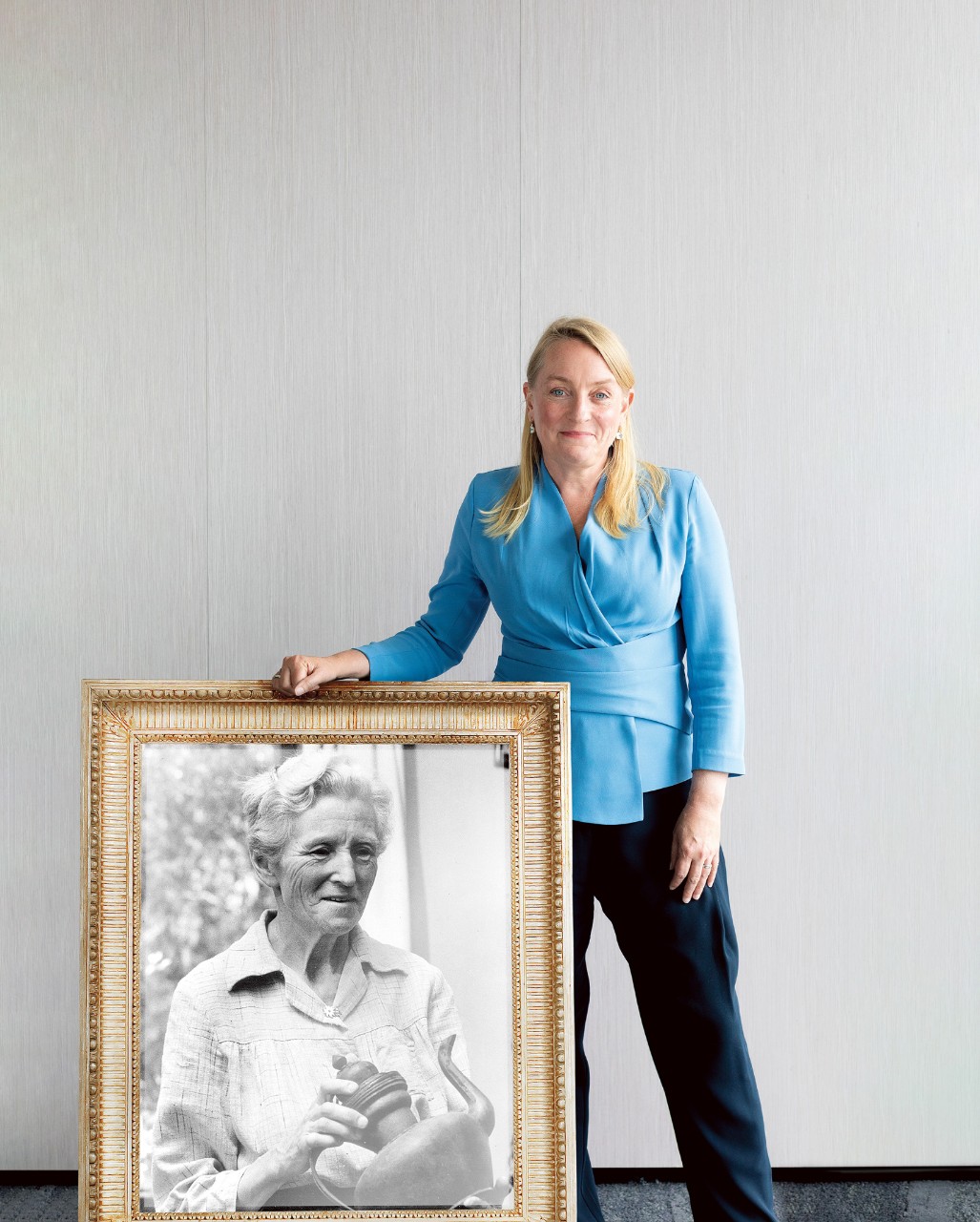 Georgia Dawson leaning against a frame with a blue blouse and black pants, inside the frame is a black and white photofraph of Marie Byles