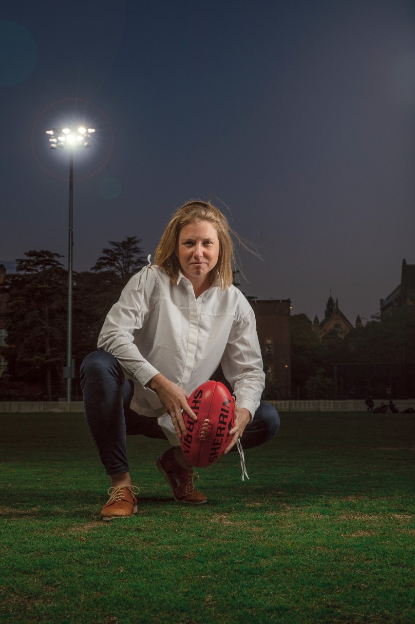 Dr Victoria Rawlings kneeling on a football field at night, holding a red football