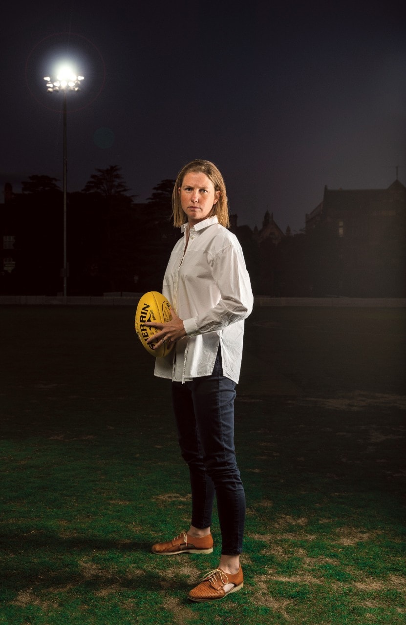Dr Victoria Rawlings standing on a football field, a yellow football in her hands