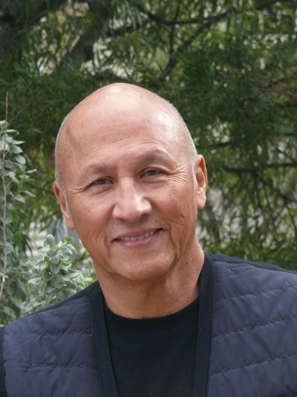 a tight headshot of a middle aged man smiling at the camera, he is bald