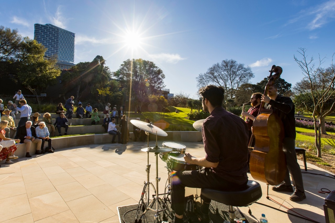 student musicians are playing drums and saxophone in an outdoors theatre in the sun