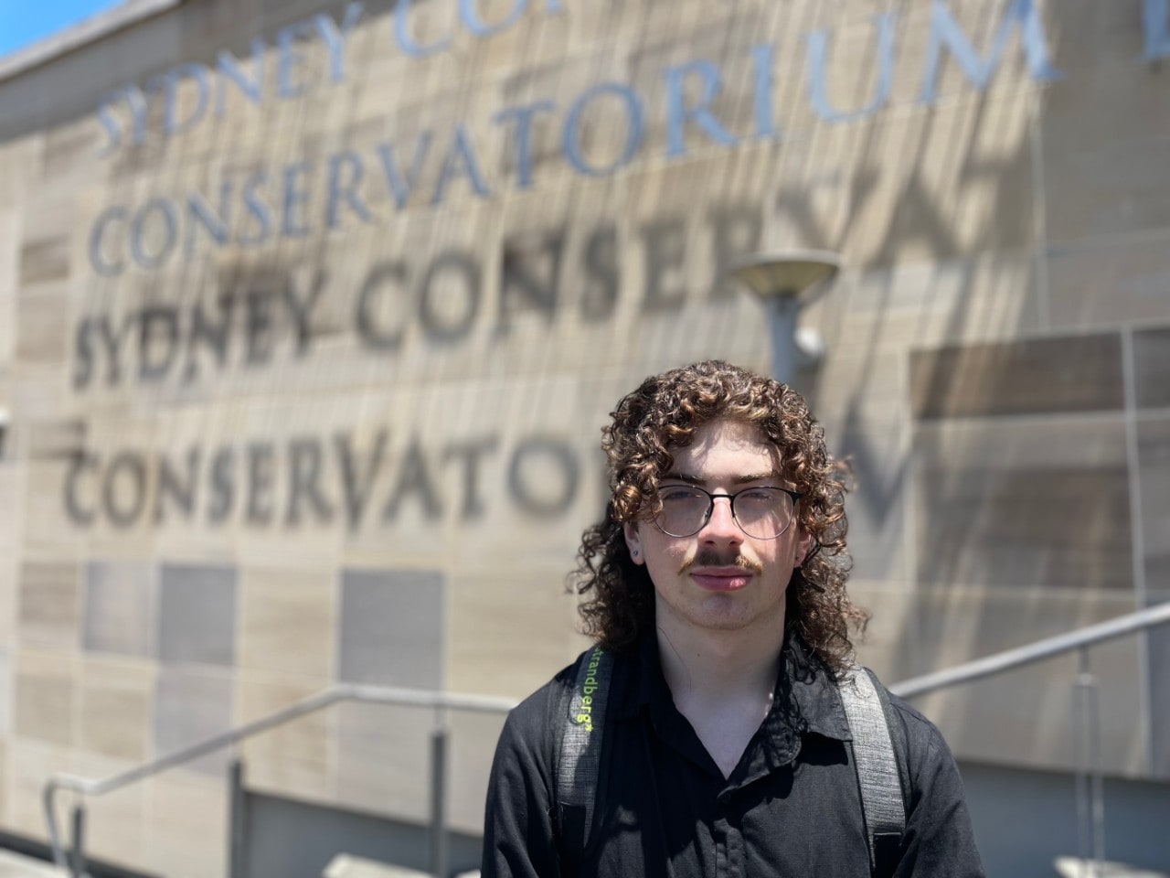 young man standing in front of the sign that says Sydney Conservatorium of Music