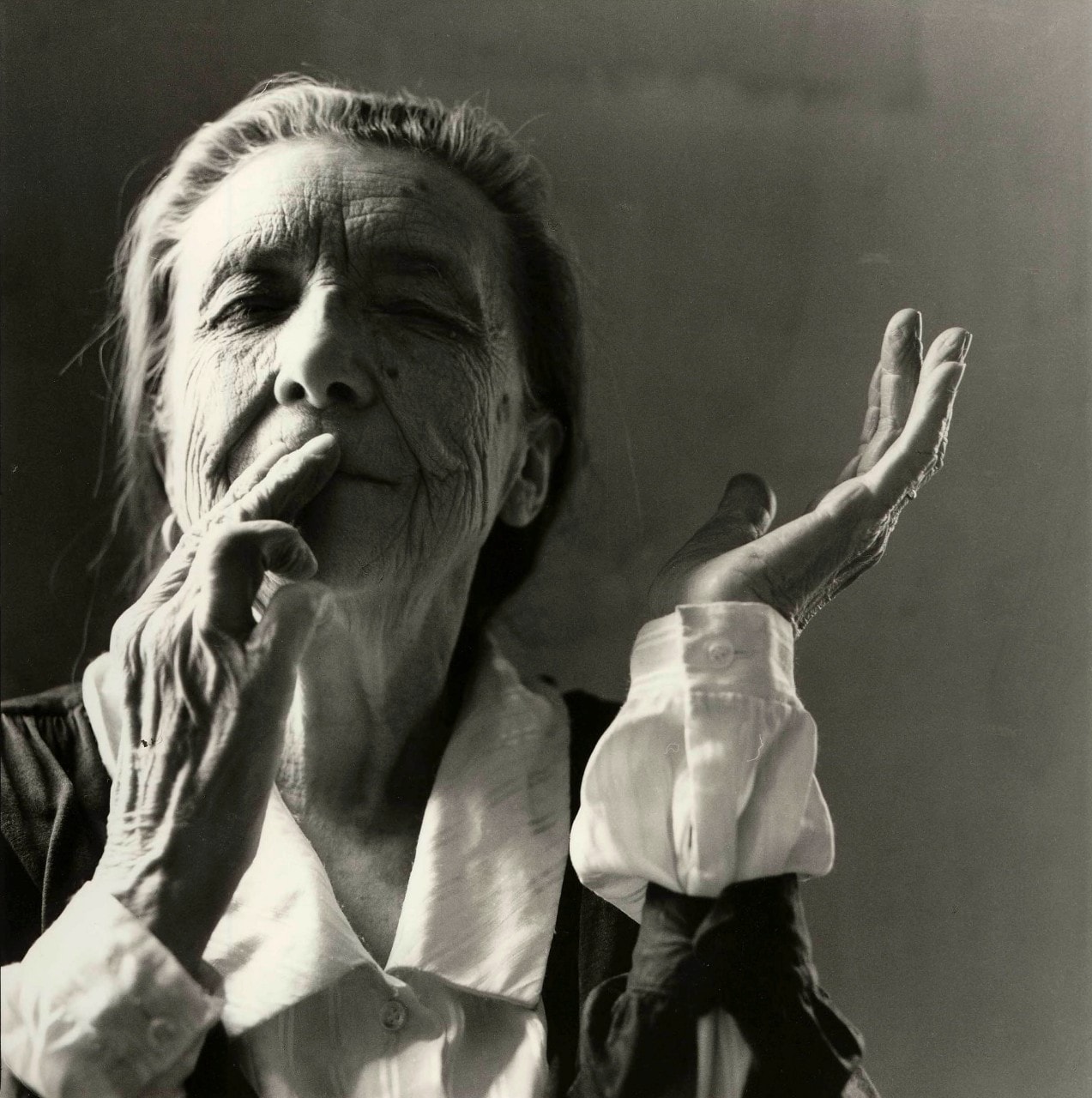 black and white photo of Louise Bourgeois, she is elderly and her hands are near her face. 