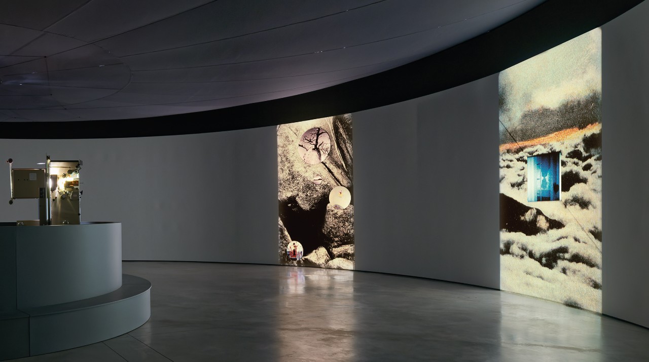 inside an art gallery room which is round, on the walls are large photos of objects on the ground with trees in the background