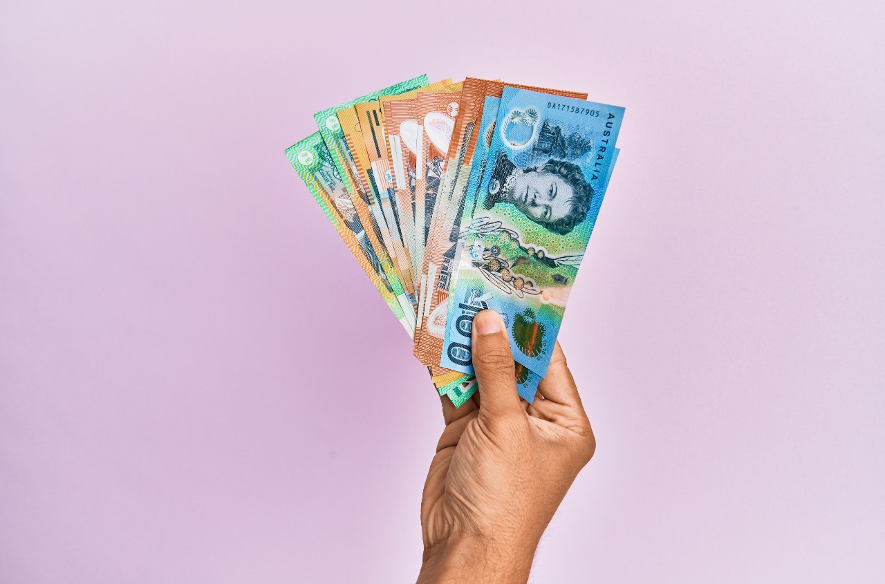 Hand holding Australian banknotes over a pink background.