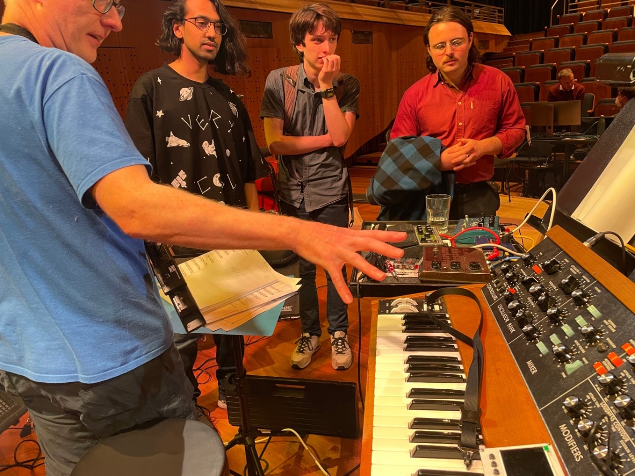 a musician pointing at a Moog keyboard with students looking on 
