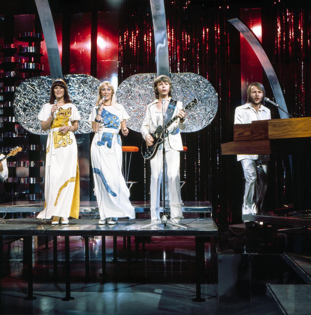 photo of ABBA, the Swedish pop group singing on stage wearing white jumpsuits.