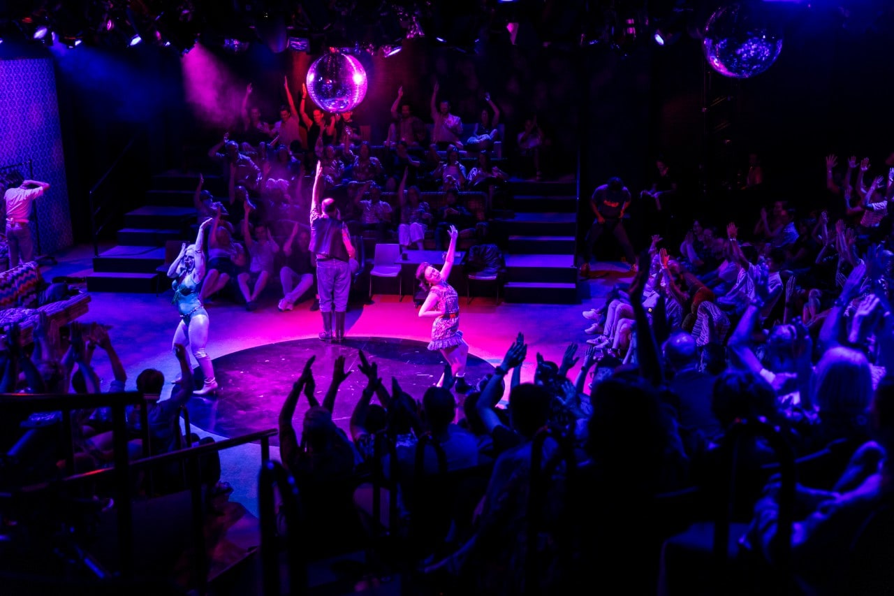 people on a stage dancing under a giant mirror ball
