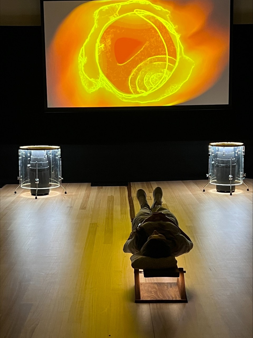 a man lying on the floor listening to sounds with a screen showing orange abstract images