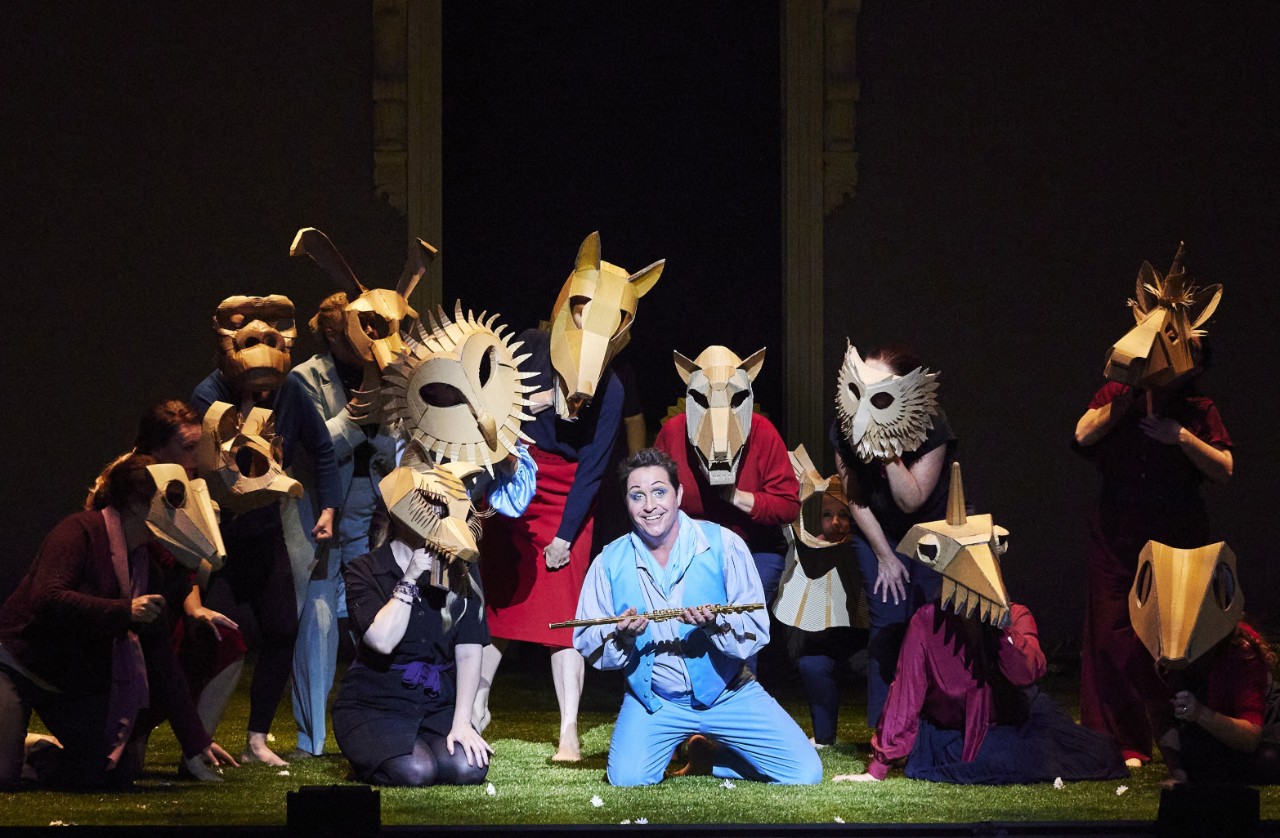 a male singer is on the floor surrounded by other singers wearing animal masks.