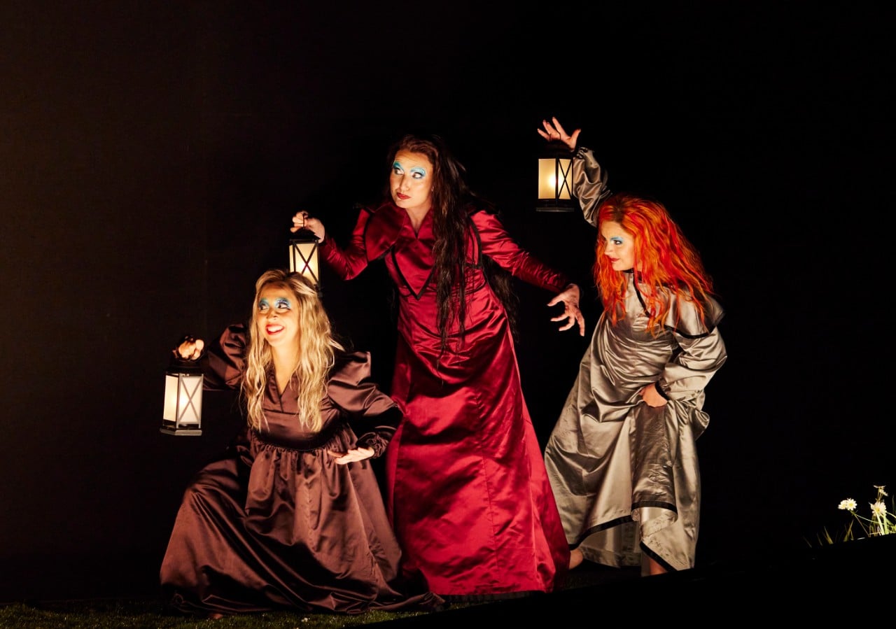 Three female opera singers in lavish red dresses