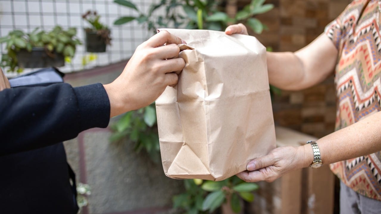 A delivery man handing over a brown paper package to a person