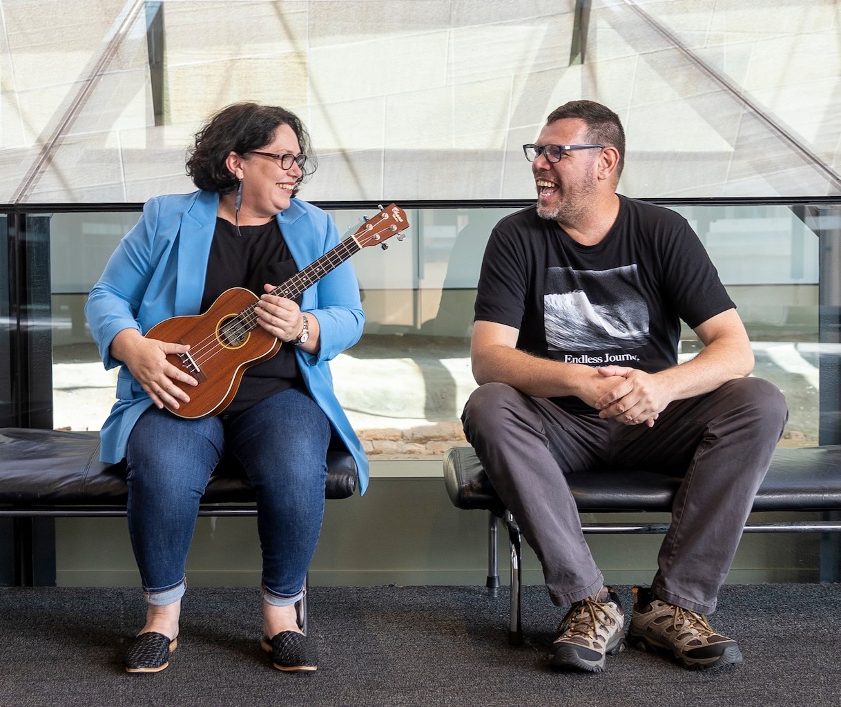a woman with a ukelele and a man sitting side by side and smiling and laughing at each other