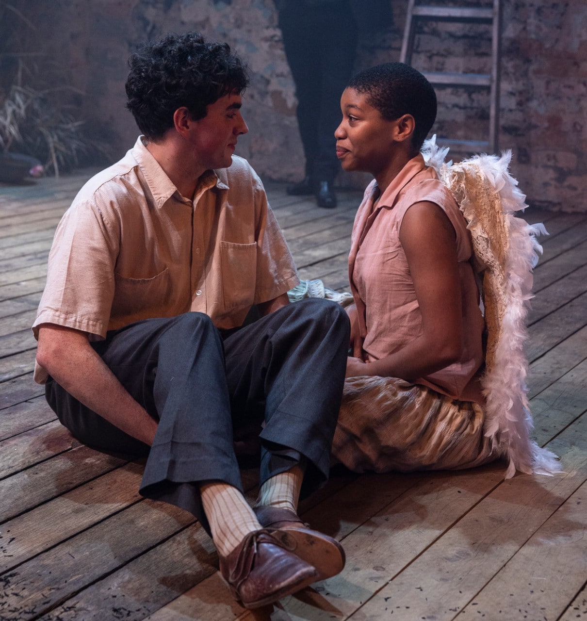 a boy and a girl sit on a wooden stage, their costumes include angel wings