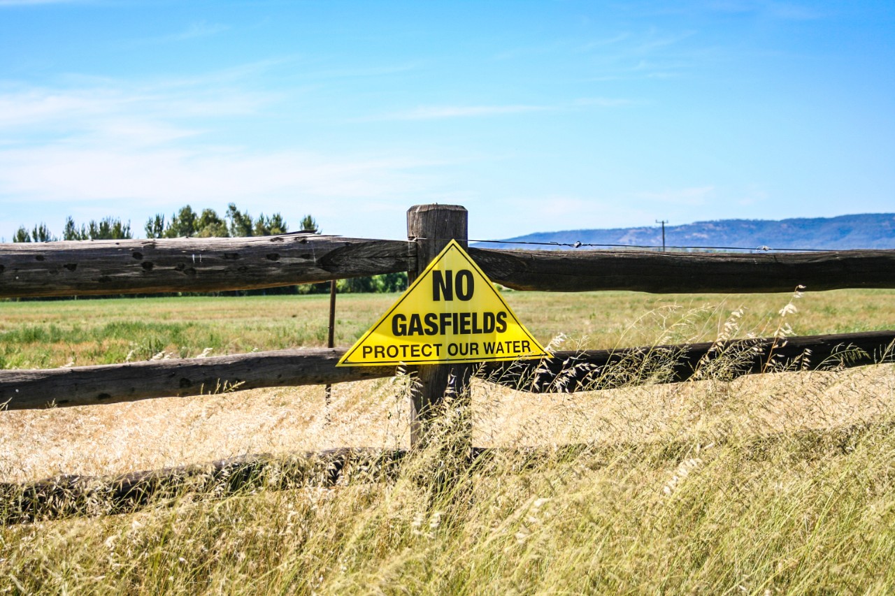 A protest sign on a wooden fence on farmland that reads 'no gasfields, protect our water'