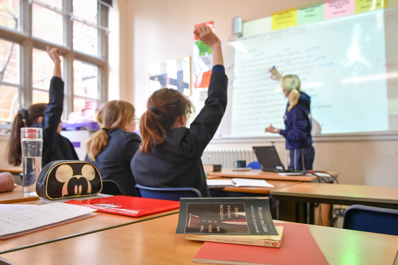 Students studying maths raising their hands to answer a question from a teacher in a classroom setting
