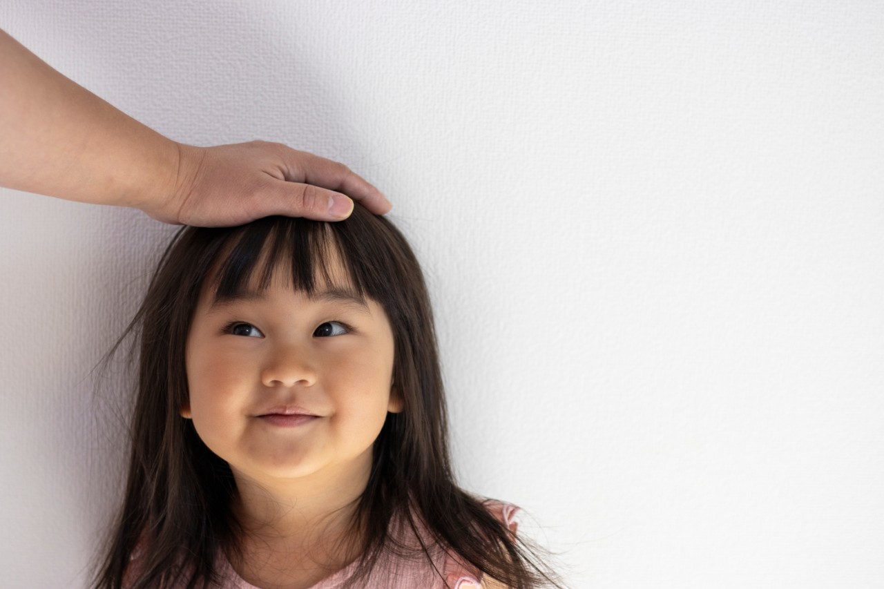A girl smiling with a hand placed on her head as if she is being congratulated