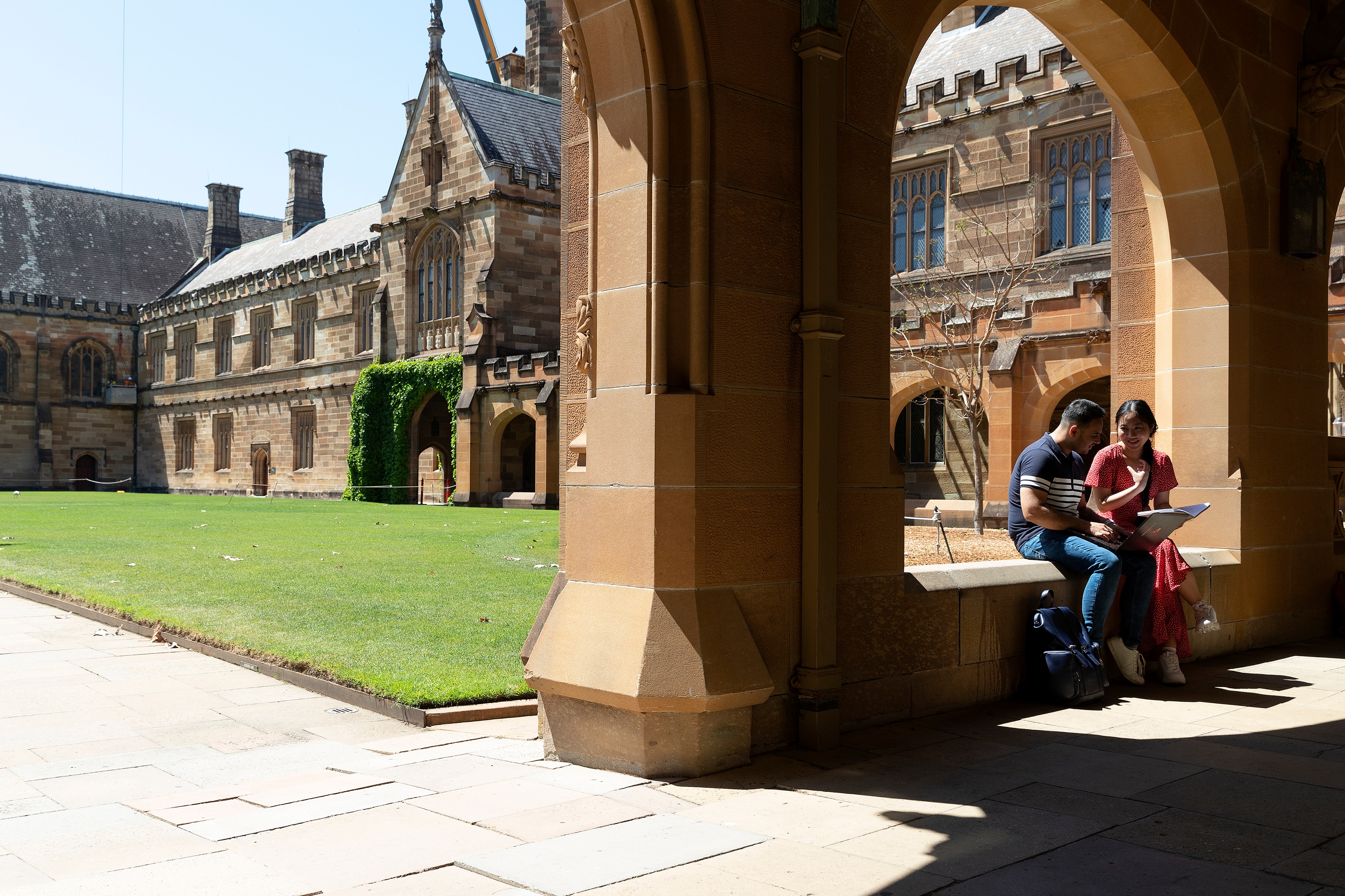 A young man and a young woman sit together under a sandstone archway in the University of Sydney Quad