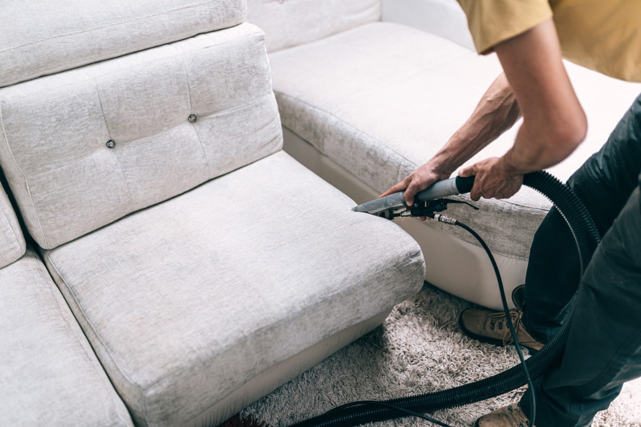 A person vacuuming the cushions on a couch.